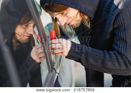 Anti theft system problem concept. Thieft man dressed in black holding screwdriver trying to break into car