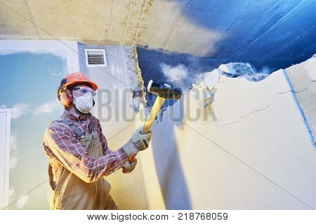 worker with sledgehammer at indoor wall destroying