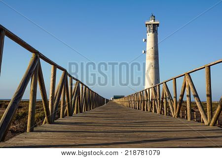 Wooden footbridge walkway to beach near Morro Jable lighthouse in warm sunset light, Fuerteventura island, Spain .