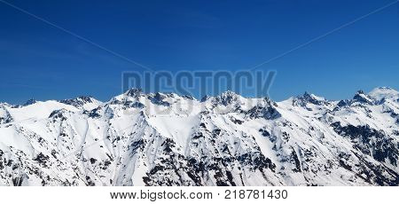 Panorama of snow covered mountains and blue sky at sun cold day. View from region Dombay Caucasus Mountains in winter.