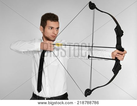 Young businessman practicing archery on light background