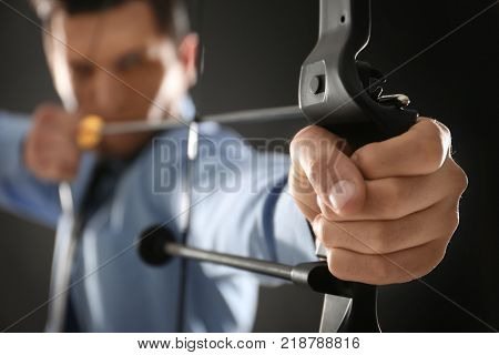 Young businessman practicing archery on dark background