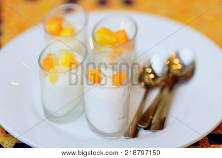 four delicious white dessert souffle with orange fruits on white plate with tea spoons