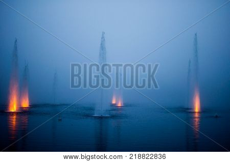 fountain in a natural lake in a foggy night with colored jets and lights