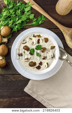 An overhead photo of a plate of a mushroom cream soup with champignons, cremini, fresh parsley, on a dark rustic background texture with a place for text