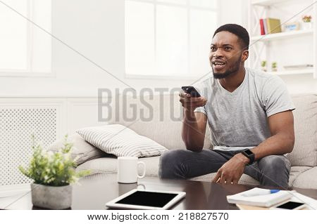 Young african-american man wathing tv. Worried guy pointing with remote controller on tv-set. Man worrying about favourite football team at home, copy space