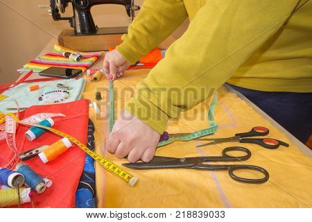Seamstress hands on the work table with measuring tape. Tailor hands working with scissor and suit textile cloth. Fashion Designer Cutting Fabric In Studio