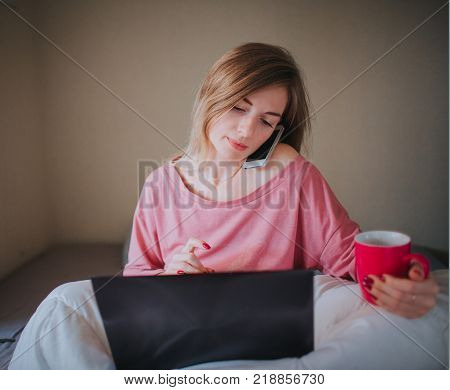 A woman works at home and drinks coffee. The concept of freelancing and multitasking.