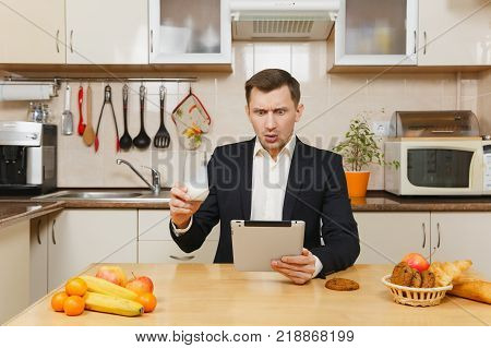 Perturbed Young Business Man In Suit, Shirt, Having Breakfast, Sitting At Table With Tablet, Spreadi
