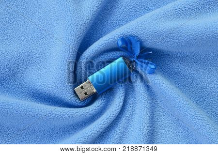 Brilliant blue usb flash memory card with a blue bow lies on a blanket of soft and furry light blue fleece fabric with a lot of relief folds. Memory storage device in women's design