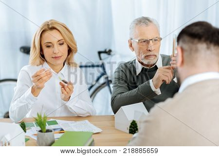 Scrupulous work. Attentive calm clever scientists being very careful while holding test tubes and looking at the tiny growing plants in them