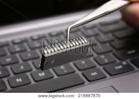 Hand with tweezers holds the chip above the keyboard of the laptop
