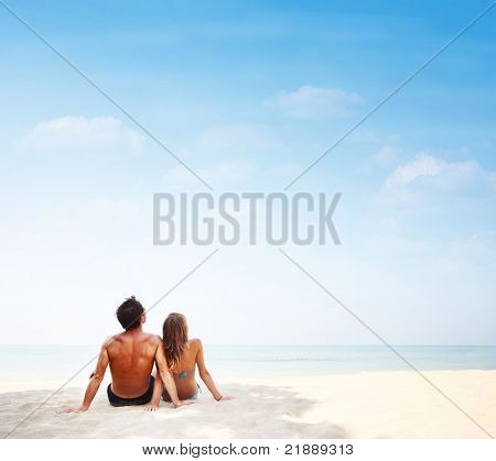 Ung familie sidder på varmt sand af et hav og leder til et sted