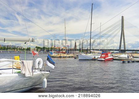 White yachts with tall masts against the panorama of the city of Riga with spiers of cathedrals and a cable-stayed bridge across the Daugava River on a summer day.