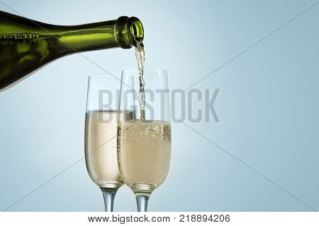 Glasses with champagne and bottle over sparkling holiday blue background