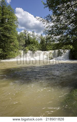 Croatian Village Of Rastoke By A River Canyon With Wooden Houses In A Green Lanscape With Trees And
