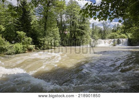 Croatian Village Of Rastoke By A River Canyon With Wooden Houses In A Green Lanscape With Trees And