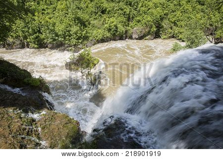 Croatian Village Of Rastoke By A River Canyon With Wooden Houses In A Green Lanscape With Trees And