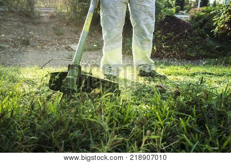 Gardener mowing the grass with lawn mower in the park. He wears Personal protective equipment (PPE)