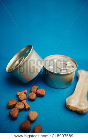 Nutritious meal for your little buddy. Tin cans of pet food and a chew bone on a bright one-color blue background. Pet care and veterinary concept. Spase for your text or image.