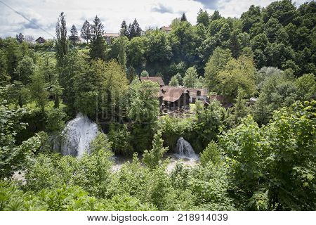 Croatian Village Of Rastoke By A River Canyon With Wooden Houses In A Green Landscape With Trees And