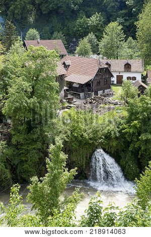 Croatian Village Of Rastoke By A River Canyon With Wooden Houses In A Green Landscape With Trees And