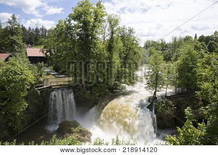 Croatian Village Of Rastoke By A River Canyon With Wooden Houses In A Green Landscape With Trees And