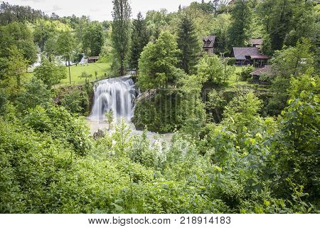 Croatian Village Of Rastoke By A River Canyon With Wooden Houses In A Green Landscape With Trees And