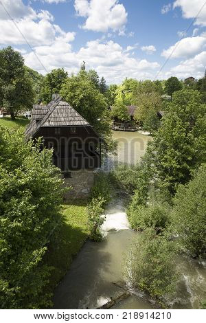 Croatian Village Of Rastoke By A River Canyon With Wooden Houses In A Green Landscape With Trees And