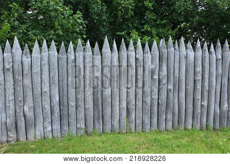 historical protecting fence from wooden logs on the green grass