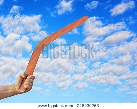 Australian Boomerang in men hand taken closeup against of cloudy blue sky.