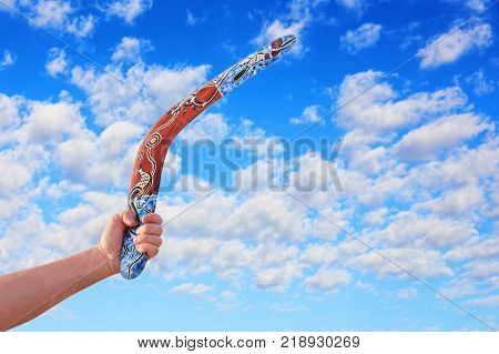 Australian Boomerang in men arm taken closeup against of cloudy blue sky.
