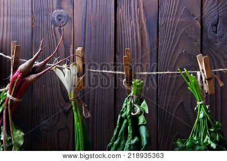 Fresh betroots, spinah, parsley green onion hanging on string.Wooden background.Concept hanging herbs.closeup