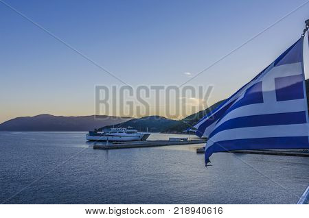 The flag of greece waving a ferry moored in the Sami Port the Ionian Sea and the mountains of the island of Kefalonia greece