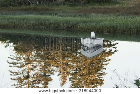 A small motor boat in a lake has a reflection that looks like it is resting on a mirror with the landscape reflection too.