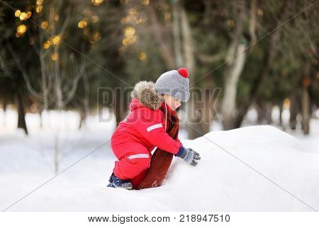 Little boy in red winter clothes having fun with fresh snow. Active outdoors leisure with children in winter. Kid during stroll in a snowy winter park
