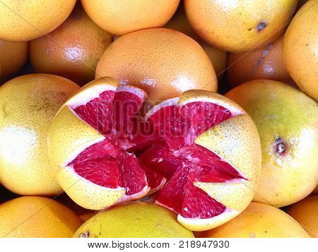 Colorful grapefruit background with many whole fruit and one sliced open with red flesh inside and space for text.