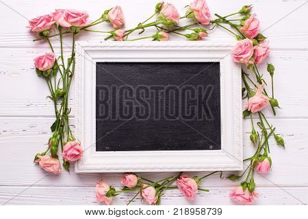 Pink roses flowers and empty blackbooard on white wooden background. Place for text. Selective focus.