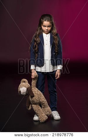 angry kid standing and holding teddy bear on burgundy
