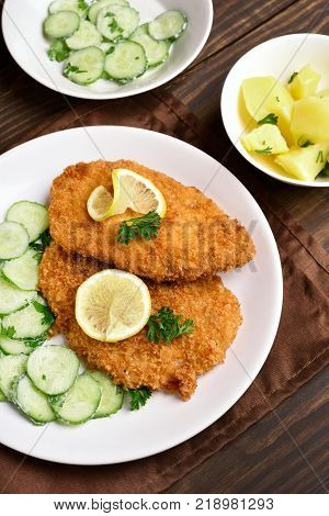 Schnitzel with cucumber salad on plate over wooden table.