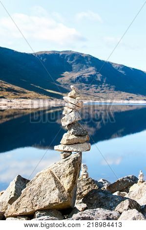 Landscape with balanced rocks in stack at beautiful scottish wild mountains and lake with reflection background. Panoramic view. Loch Cluanie fort William. Scotland. Uk. Vibrant colored summertime outdoors vertical image with cloudy sky