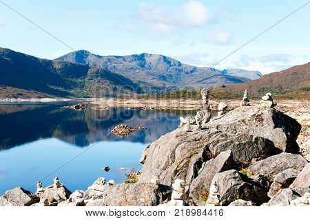 Landscape with balanced rocks in stack at beautiful scottish wild mountains and lake with reflection background. Panoramic view. Loch Cluanie fort William. Scotland. Uk. Vibrant colored summertime outdoors horizontal image with cloudy sky