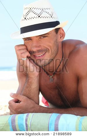 Uomo muscoloso in un cappello di paglia sdraiato sulla spiaggia