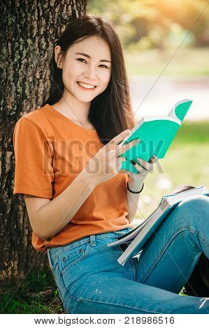A young or teen asian girl student in university smiling and reading the book and look at the tablet or labtop computer in summer holiday.