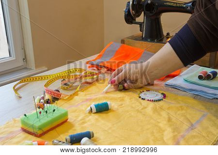 Couturier sews a dress in the studio. Fashion designer making a pattern on a red piece of tissue. Sewing machine is standing on the table beside them