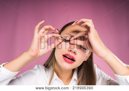 young girl on a pink background apply false eyelashes