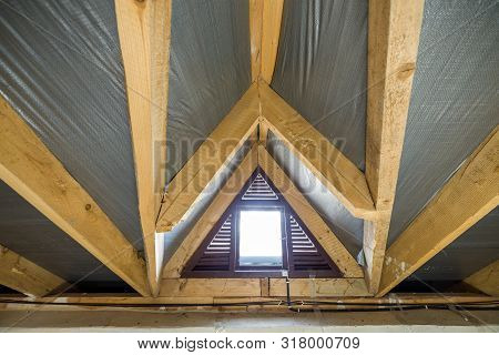Attic Of A Building With Wooden Beams Of A Roof Structure And A Small Window.