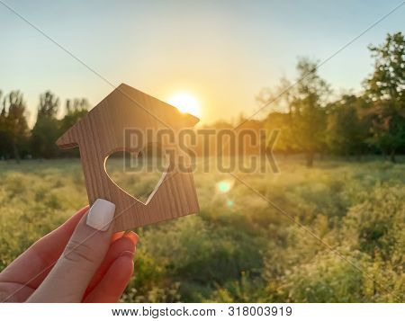 Miniature Wooden House In The Shape Of A Heart In The Hands Of A Girl Outdoors. Real Estate Concept.