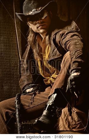 Cowboy with Black Leather Flogging Whip in his hand against wooden background