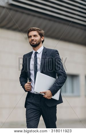Businessman In Suit With  Laptop  In His Hand Goes To Work On The Road To The Entrance Of A Glass Of